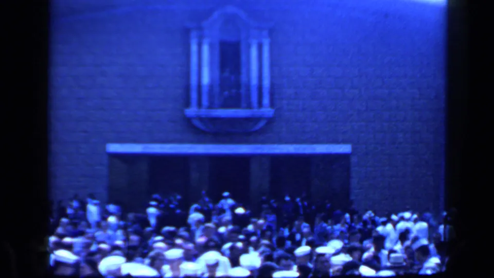 1960 Rome 8mm frame showing a dense crowd, many white hats, and a building facade with an arched window above a broad entrance.