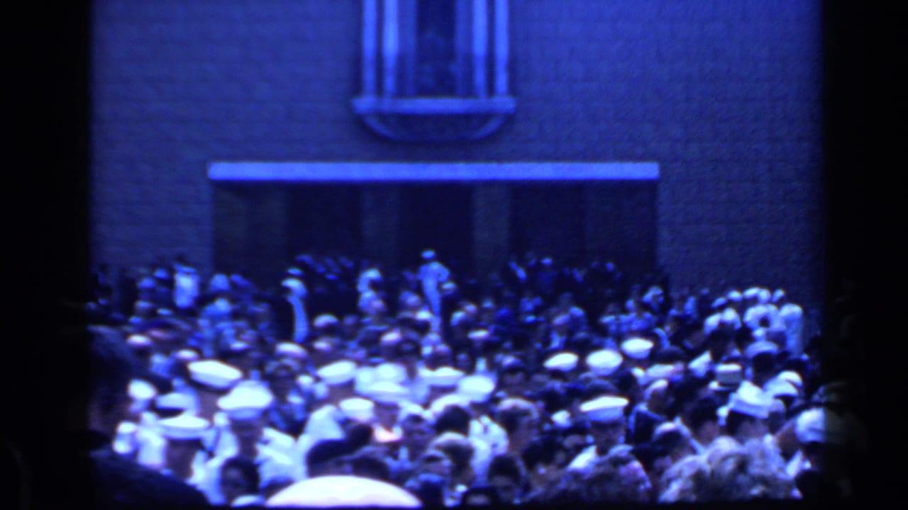 Crowd gathered outside a stone building entrance with many white caps visible.