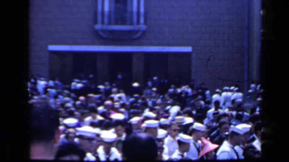 Rome, 1960 footage shows a packed crowd outside a building, with uniformed men in white caps mixed among civilians.