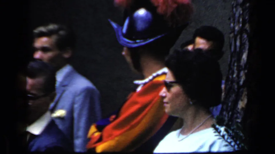 Close 1960 Rome crowd frame with adults near a wall and a costumed figure wearing a bright cape and dark hat.