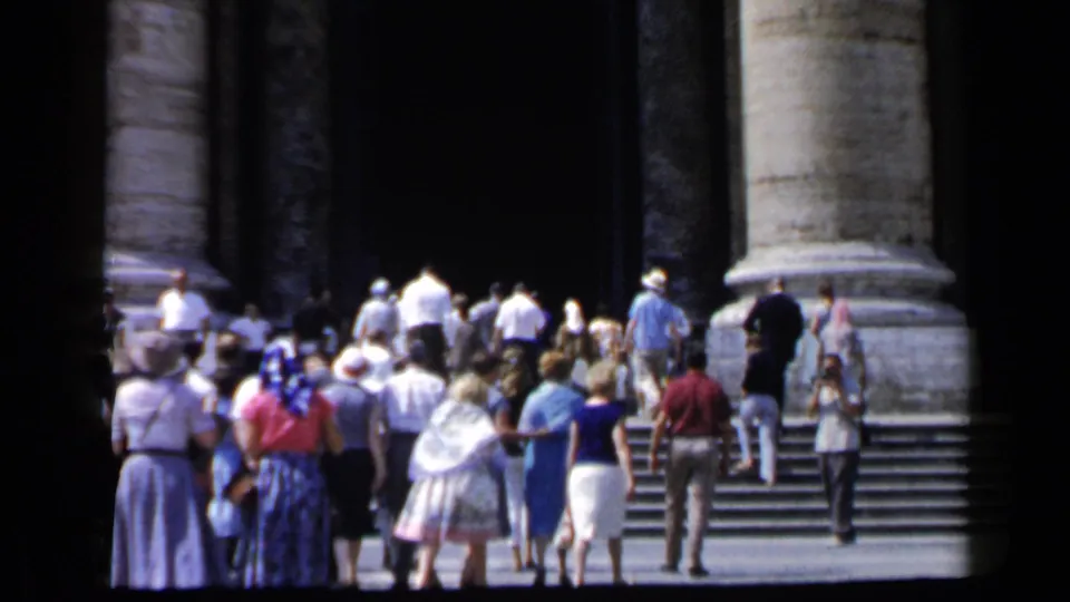A 1960 Vatican travel frame shows tourists from behind walking up broad steps toward monumental stone columns.