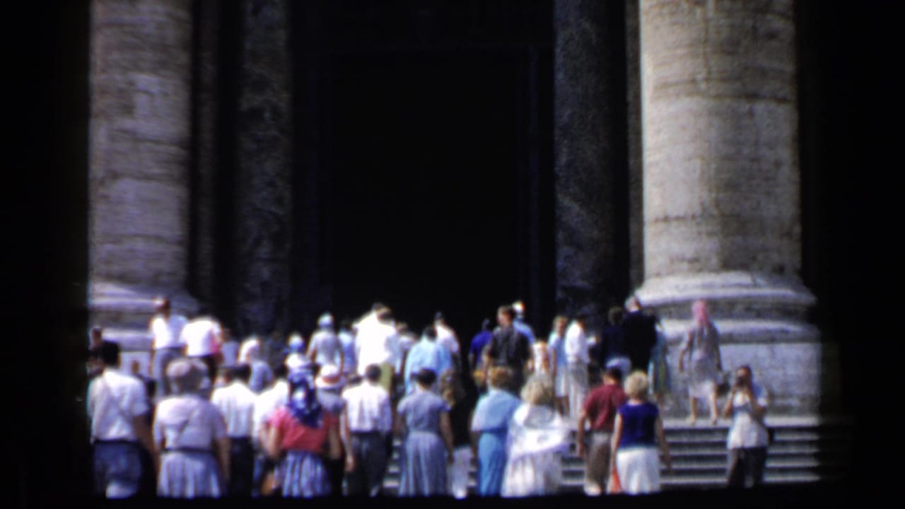 Crowd of visitors walking up steps beneath large stone columns.