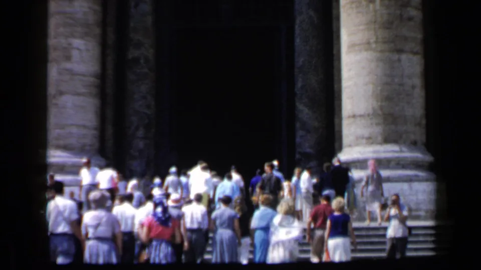 1960 Vatican home-movie frame showing visitors ascending steps near the basilica entrance beneath monumental columns.