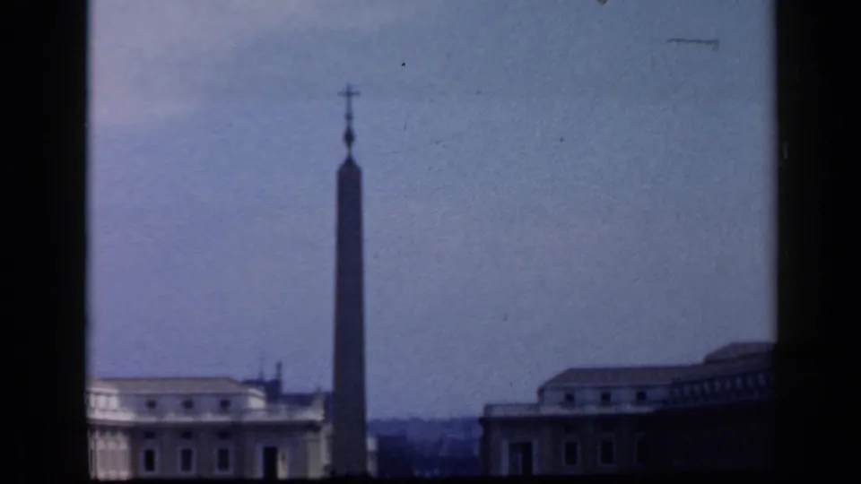 1960 Vatican frame centered on the St. Peter's Square obelisk, with surrounding buildings and a pale sky in soft 8mm color.