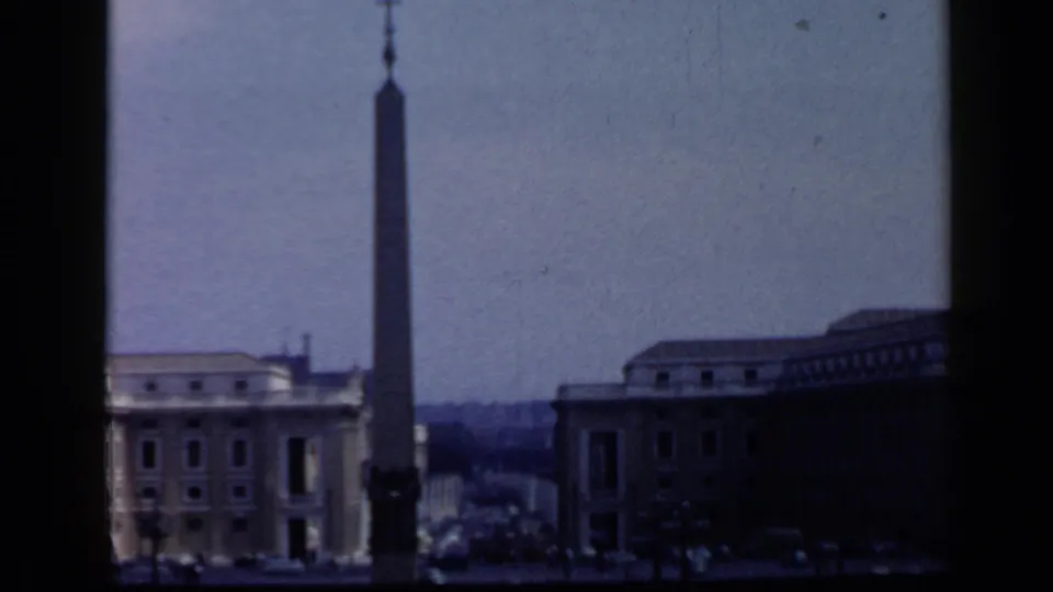 1960 Vatican home-movie frame showing the obelisk and surrounding square buildings, partially framed by a dark vertical edge.