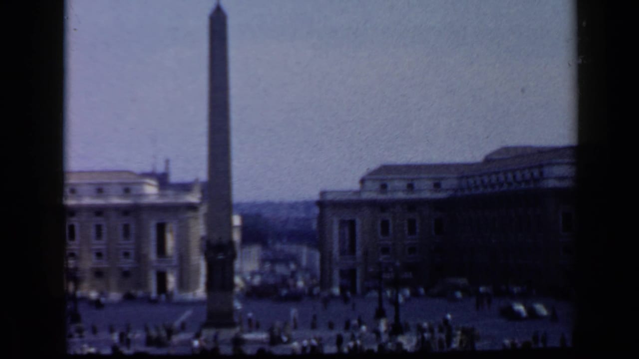 St. Peter's Square with the obelisk, Vatican buildings, and distant pedestrians.