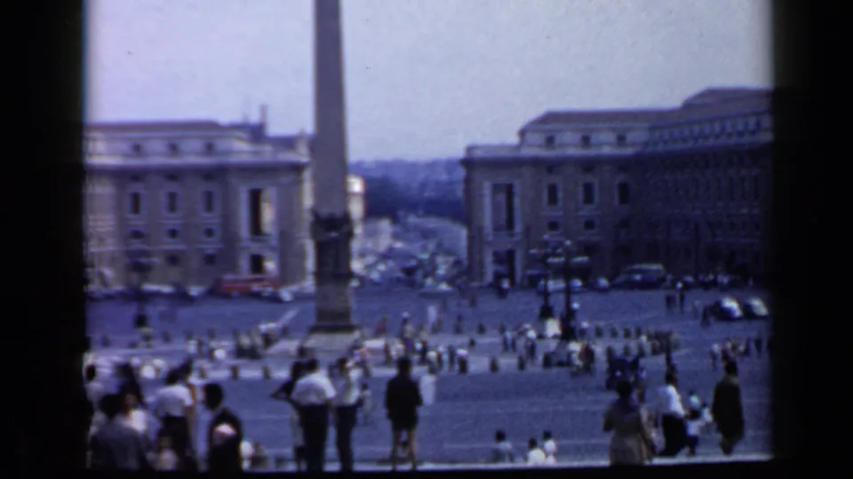 Visitor-shot 1960 Vatican view with the St. Peter's Square obelisk, pedestrians in the plaza, parked cars, and surrounding architecture.