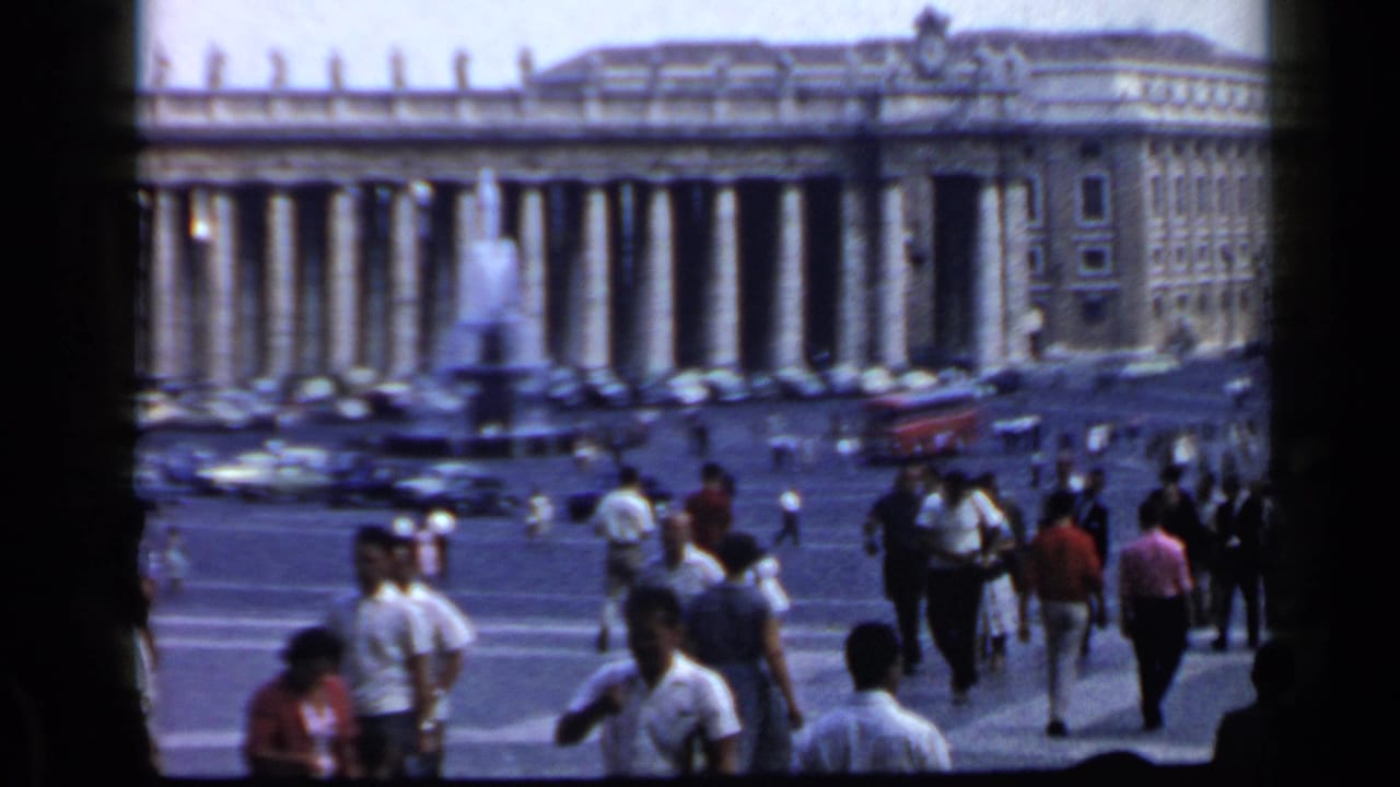 Crowds walk across St. Peter's Square with a fountain and colonnade behind them.