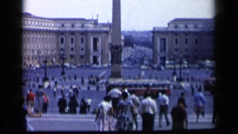 Wide 1960 Vatican City view toward the central obelisk, with visitors, buses, lampposts, and surrounding buildings in the square.