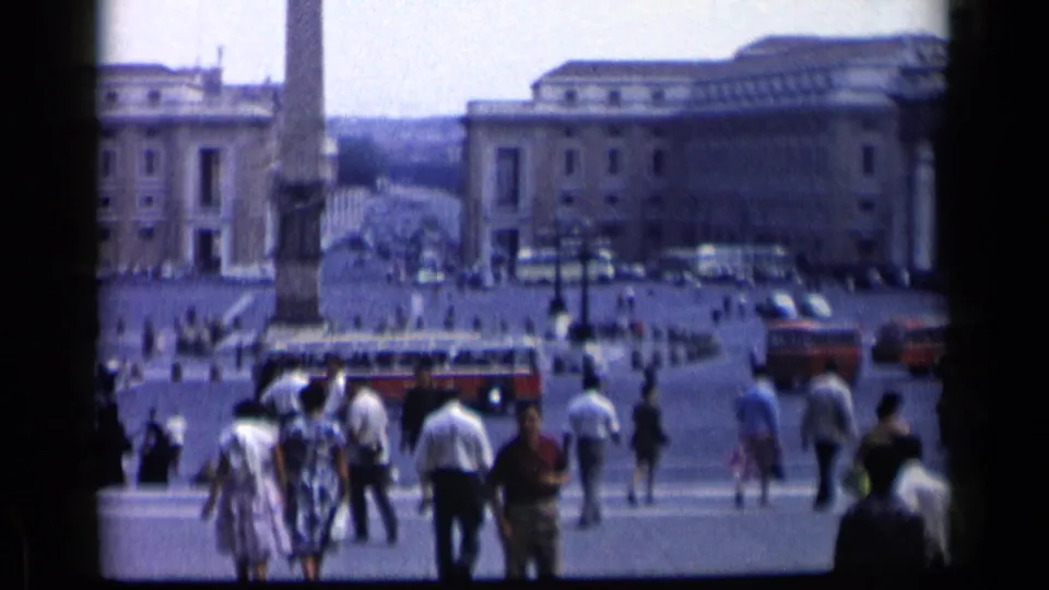 Hand-held 8mm view of St. Peter's Square in 1960, showing pedestrians near the obelisk, tour buses, lampposts, and Vatican buildings.