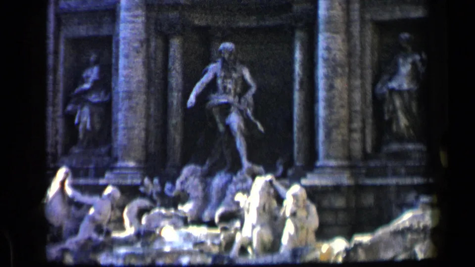 1960 8mm view of Rome's Trevi Fountain, showing sculpted figures, columned niches, water, and distant visitors in the foreground.