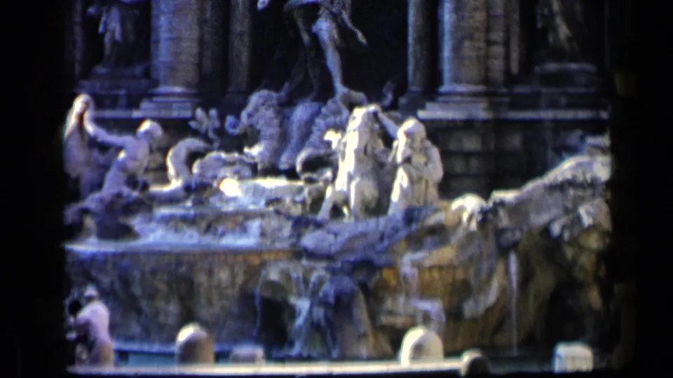 1960 8mm frame showing the Trevi Fountain's stone figures, basin edge, and several distant visitors near the lower border.