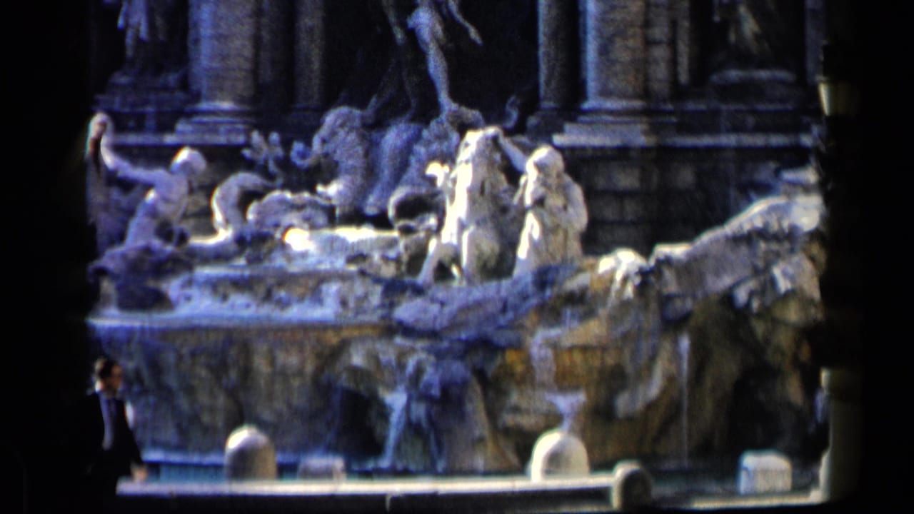 1960 8mm view of Rome's Trevi Fountain, showing stone sculptures, cascading water, and tourists at the lower edge.