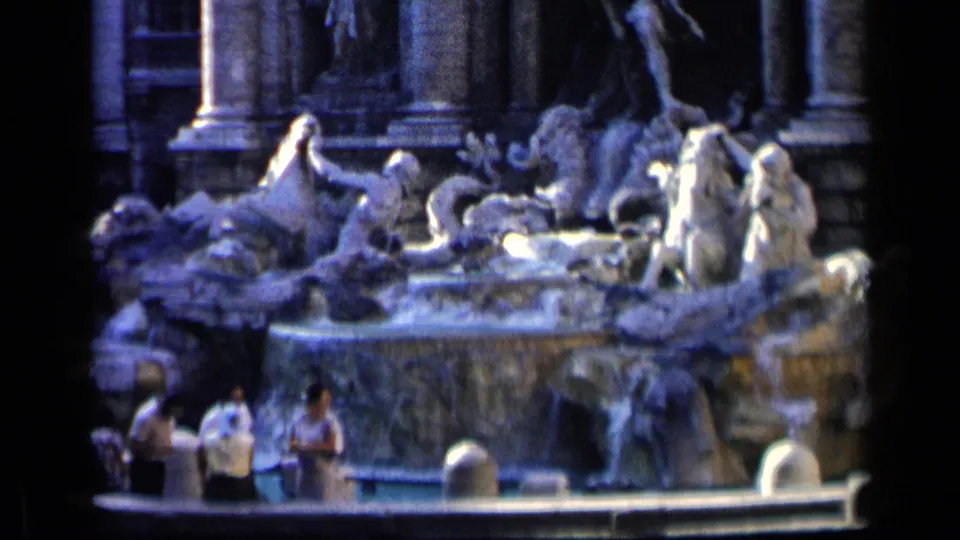 Soft 8mm frame of Rome's Trevi Fountain, showing the rocky basin, sculpted figures, water, and visitors near the foreground.