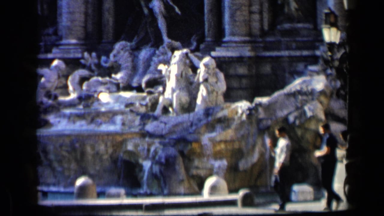 Sculpted fountain with water and pedestrians crossing the foreground.