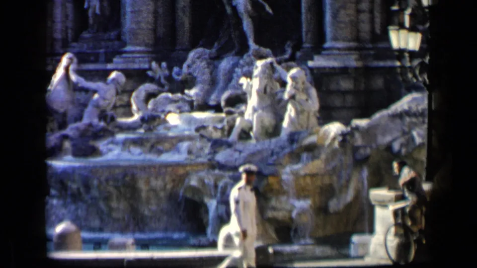 1960 Italian public fountain view with a white-uniformed man and civilian movement in the foreground.