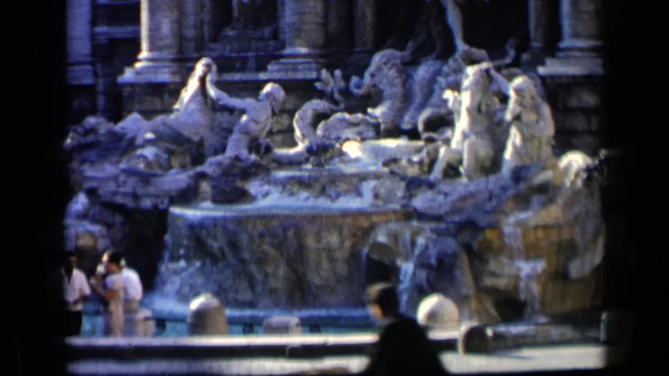 Tourists in light clothing gather at the Trevi Fountain in Rome, framed by sculpted figures, columns, and bright falling water.