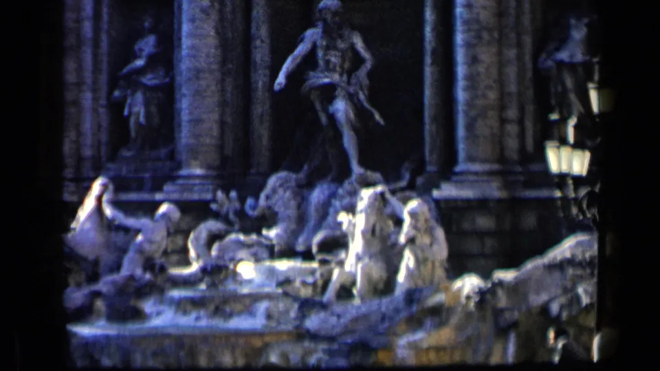 Circa-1960 8mm view of Trevi Fountain statuary in Rome, with stone figures, columns, water, and a lamp in handheld framing.