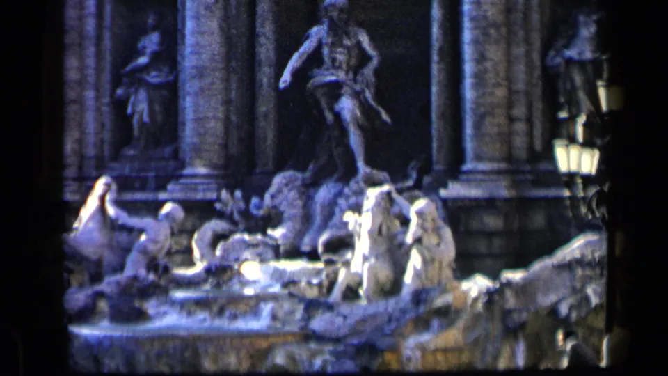 A softly focused 8mm view of Trevi Fountain stone figures, columns, water, and a lamp, consistent with the Rome travel footage metadata.