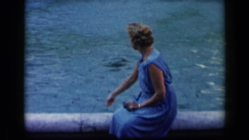 1960 Vatican, Italy home-movie frame of a woman in a blue dress reaching toward the water, possibly feeding fish.