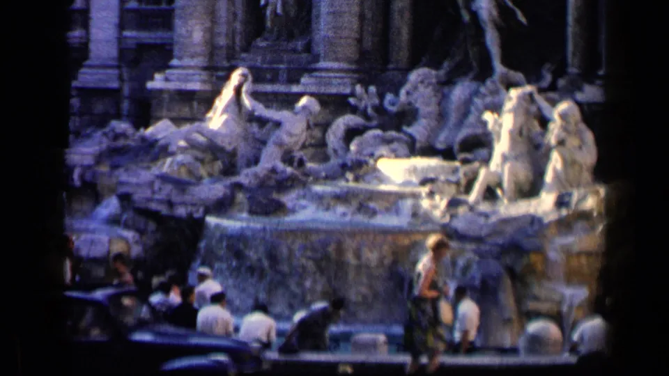 1960 8mm Rome scene with the Trevi Fountain, tourists at the basin, and a dark automobile in the foreground.