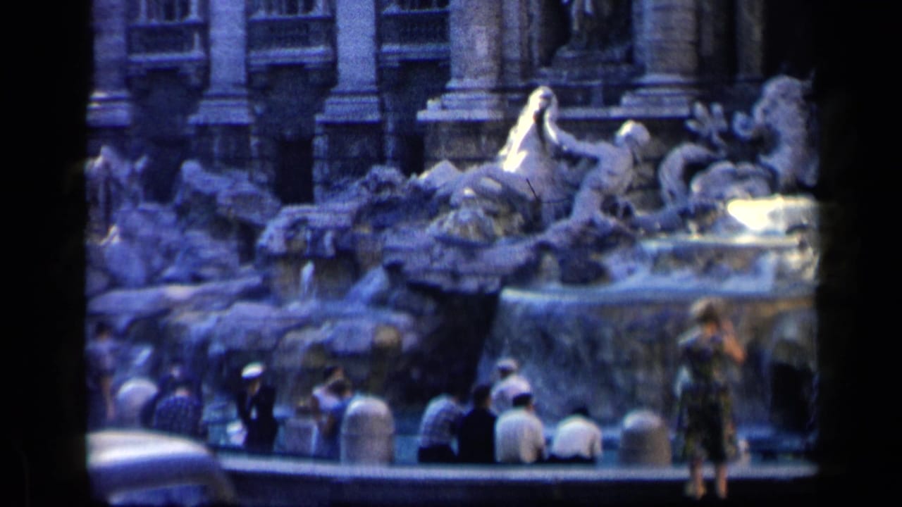 1960 8mm view of tourists at Rome's Trevi Fountain, with visitors seated and standing near the stone rim.
