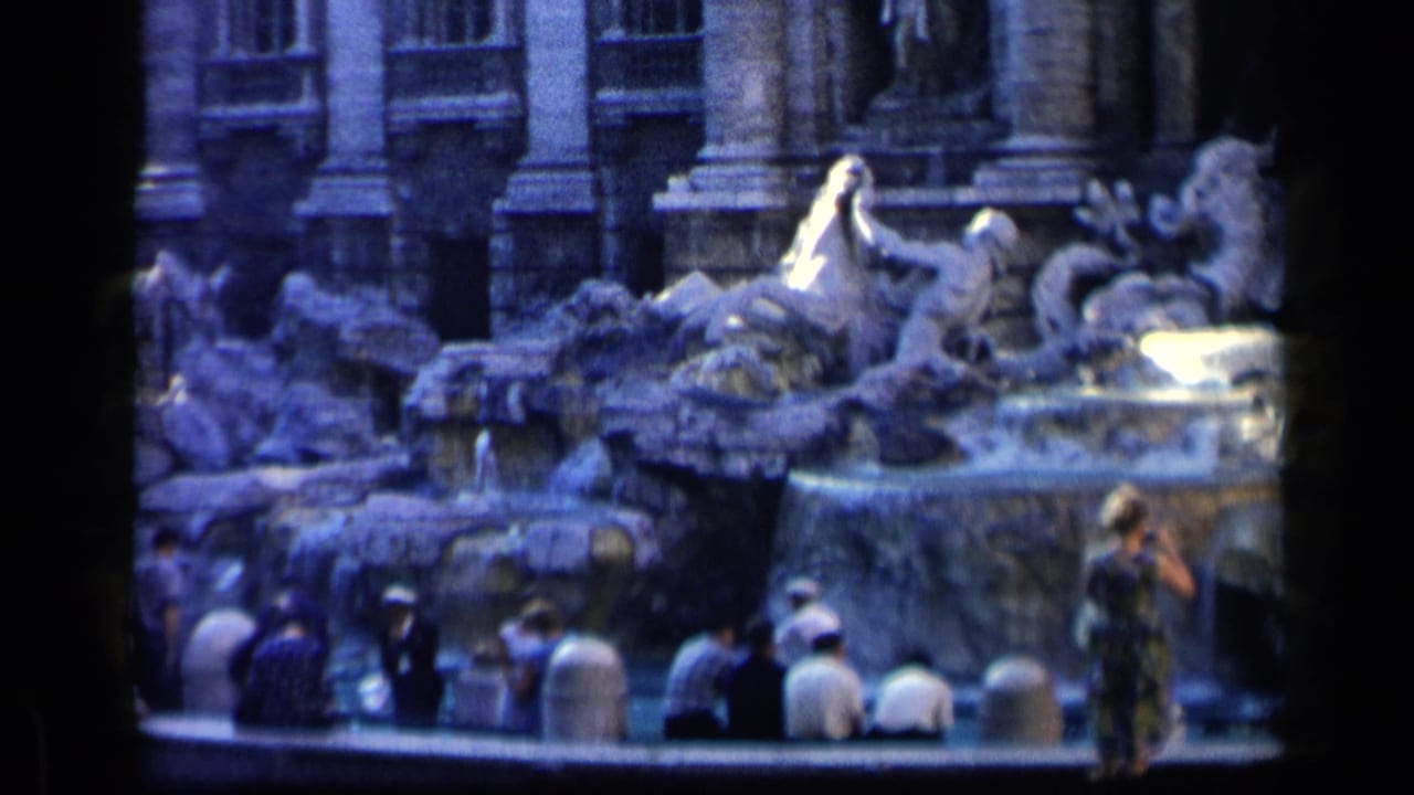 Tourists in mid-century clothing pause at the Trevi Fountain in Rome, some seated along the edge and one standing near the water.