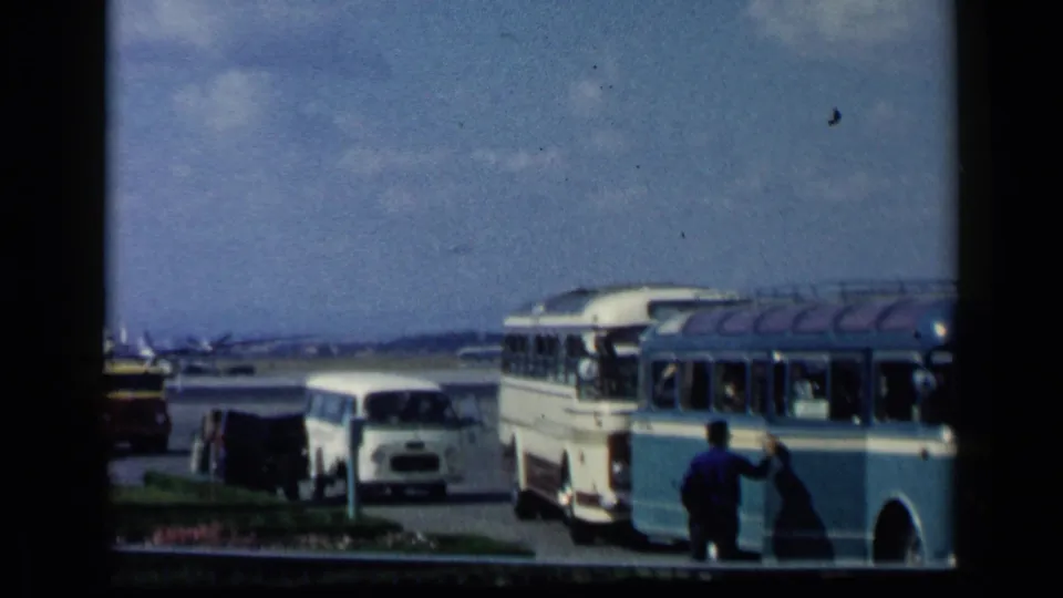 1960 Italy travel footage shows a man by a blue and white bus, with a white van, yellow bus, and aircraft on the tarmac.