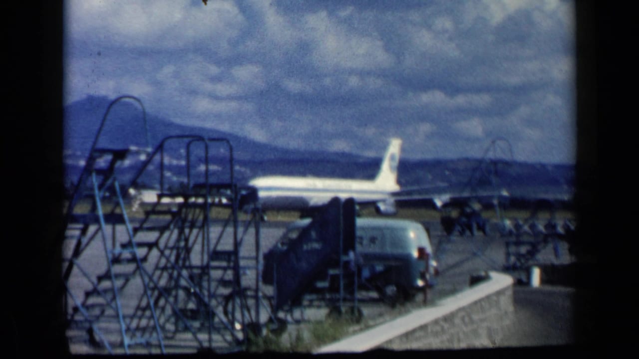 Pan Am jetliner on airport tarmac behind metal stairs and a service van.