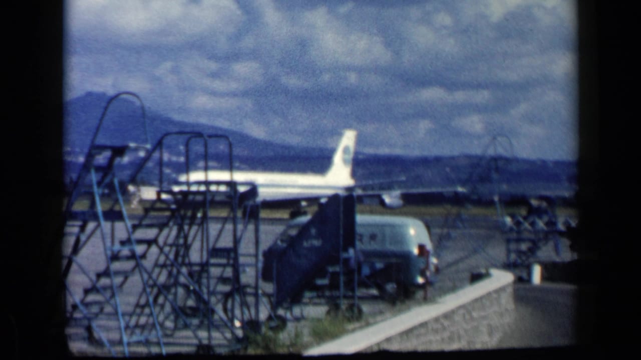 The Pan Am Boeing 707 appears on the tarmac in Vatican, Italy, with boarding stairs, service vehicles, hills, and cloud cover in view.