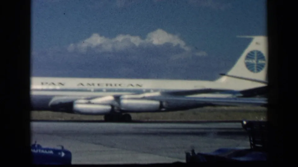 1960 archival 8mm frame with the Pan American name and globe tail logo visible on a jet at the runway.