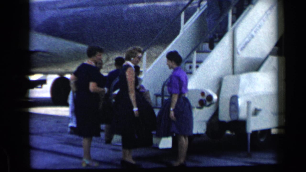 Women with luggage stand on the tarmac beside a mobile airplane stairway.