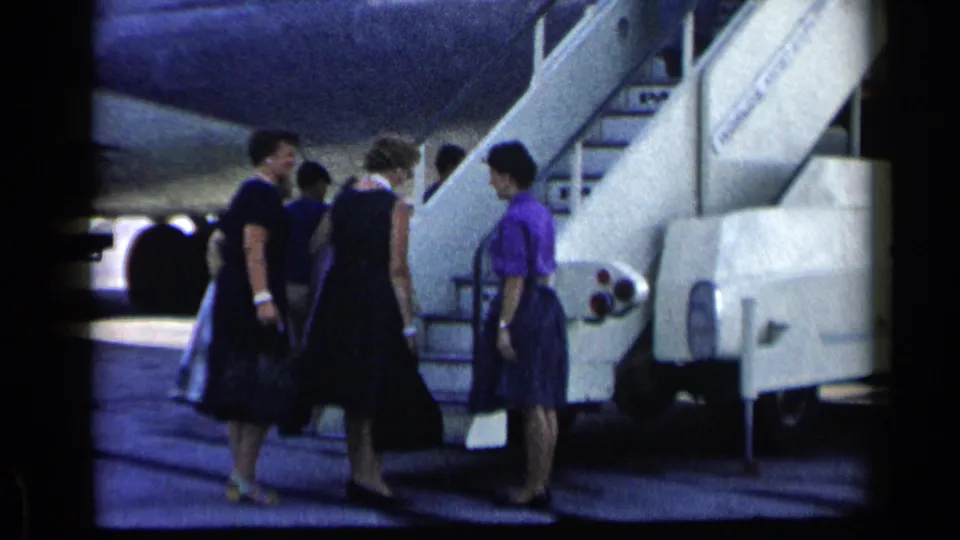 Women and other passengers approach a mobile airplane stairway with bags in 1960 Vatican, Italy metadata context.