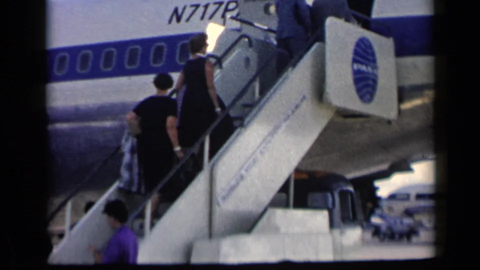 Passengers ascend mobile stairs to a commercial airplane with a partially visible registration and airline marking.