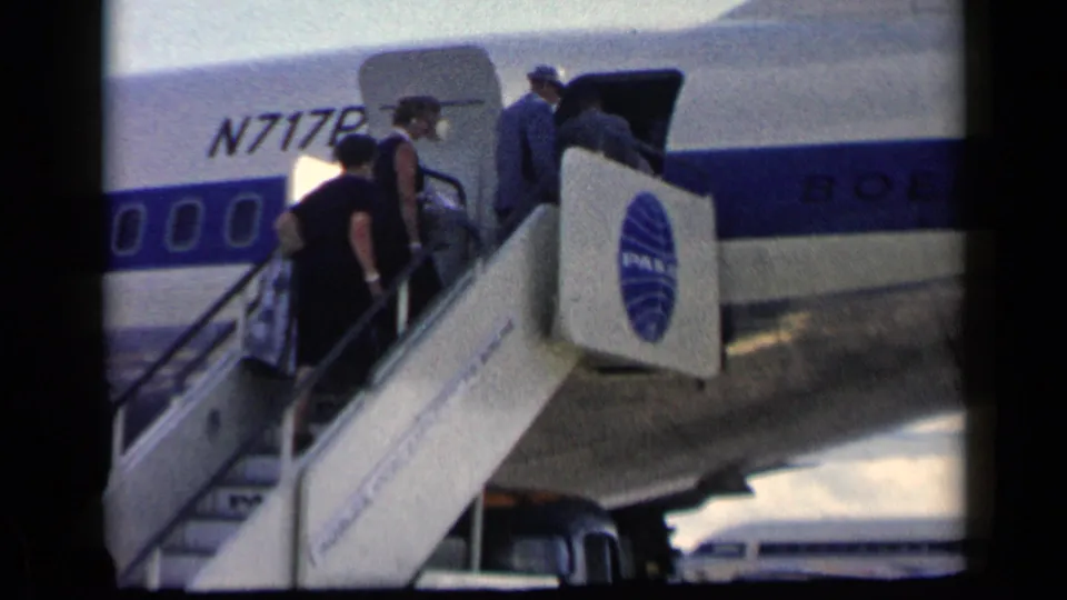 The handheld 8mm frame shows travelers moving up the stairway toward the Pan Am aircraft door, with N717P partly visible.