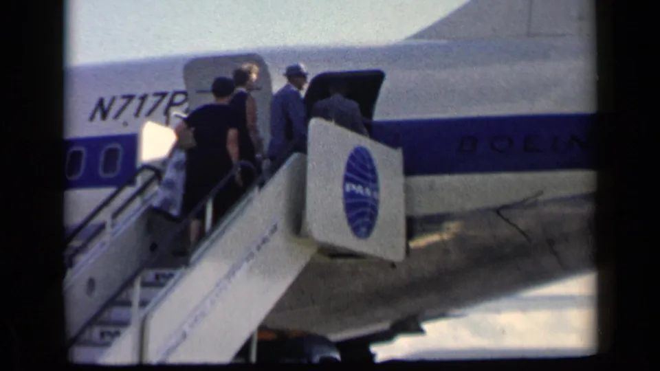 A small group of passengers boards the Pan Am Boeing airliner by mobile stairs, with the open cabin door and registration visible.