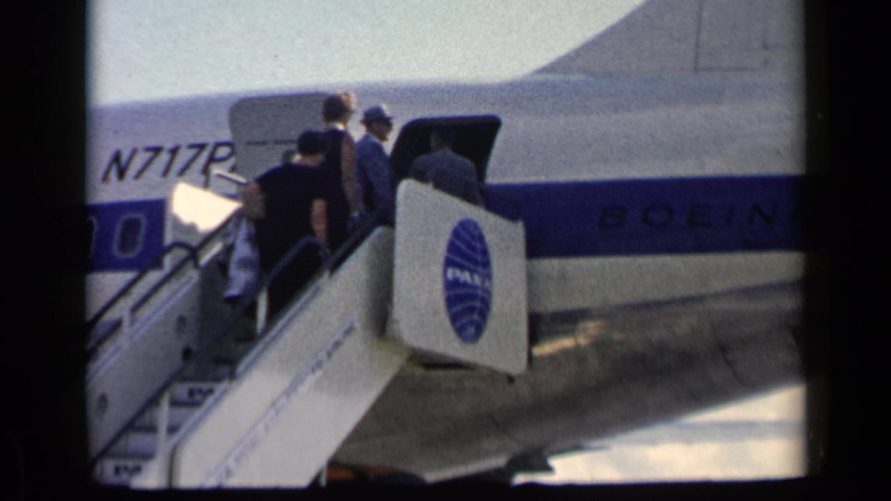 Passengers climb mobile stairs toward an open Pan Am Boeing aircraft door.