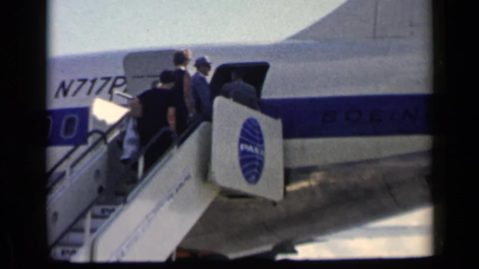 In 1960 home-movie footage, several passengers board a Pan Am Boeing aircraft by mobile stairs on an airport tarmac.