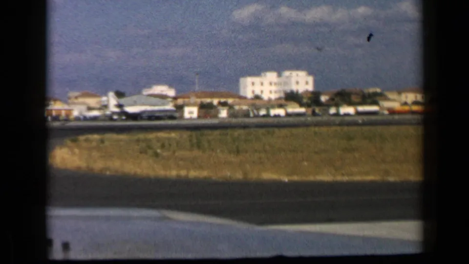 Soft 8mm frame of a commercial aircraft near airport buildings in the reported 1960 Vatican, Italy travel footage.