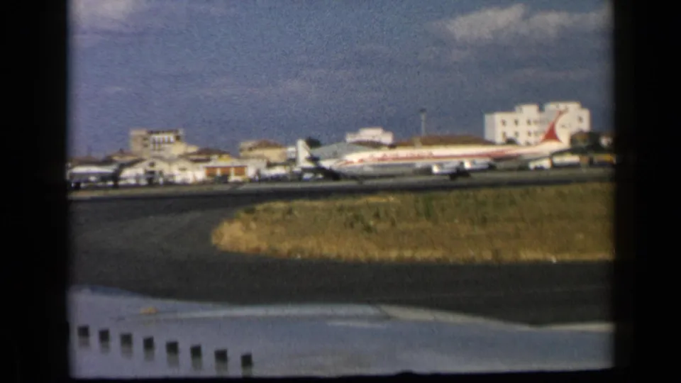 1960 8mm frame showing a commercial jet with visible livery near a runway in the reported Vatican, Italy airport scene.