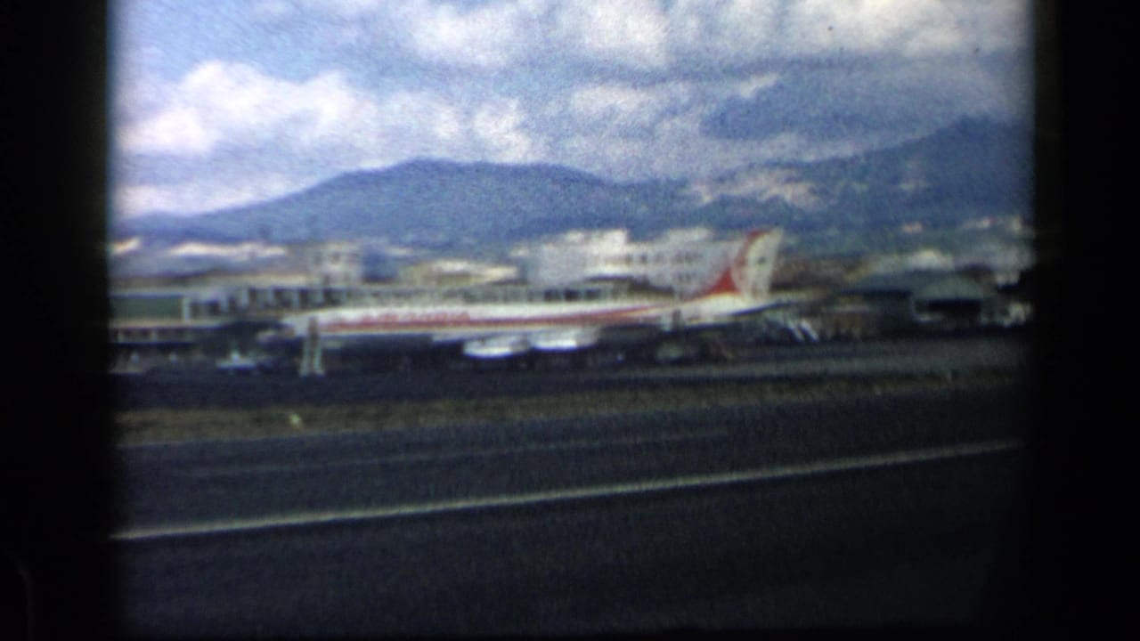 Commercial airplane on a runway with terminal buildings and mountains behind it.
