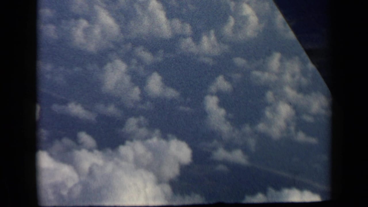 Blue sky and white clouds seen through a dark airplane window frame.