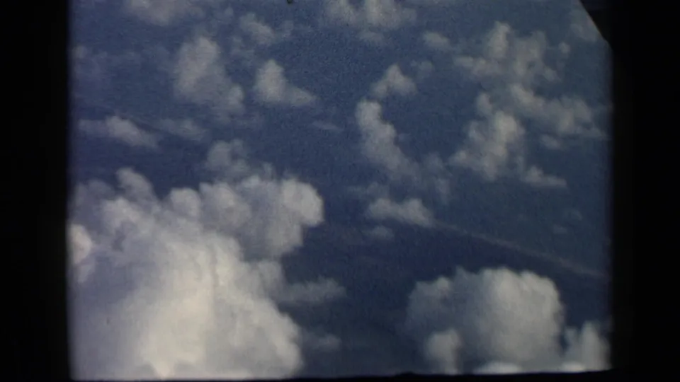 1960 8mm airplane-window view of bright cumulus clouds against blue sky, with heavy dark borders from the cabin or film gate.