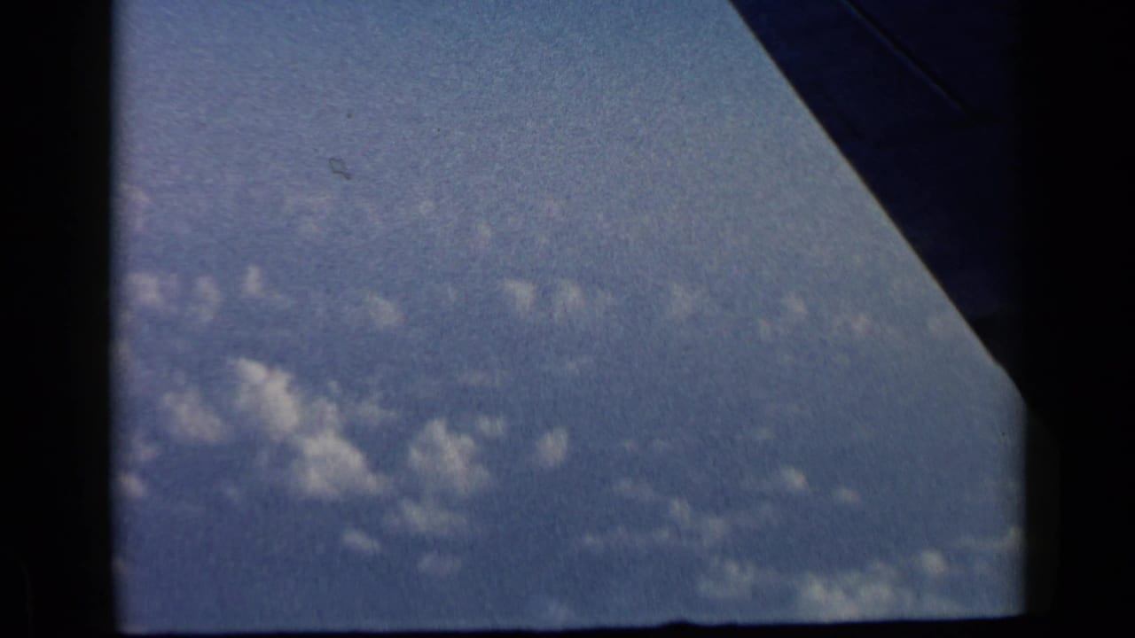 Blue sky and scattered clouds seen through a dark airplane window frame.