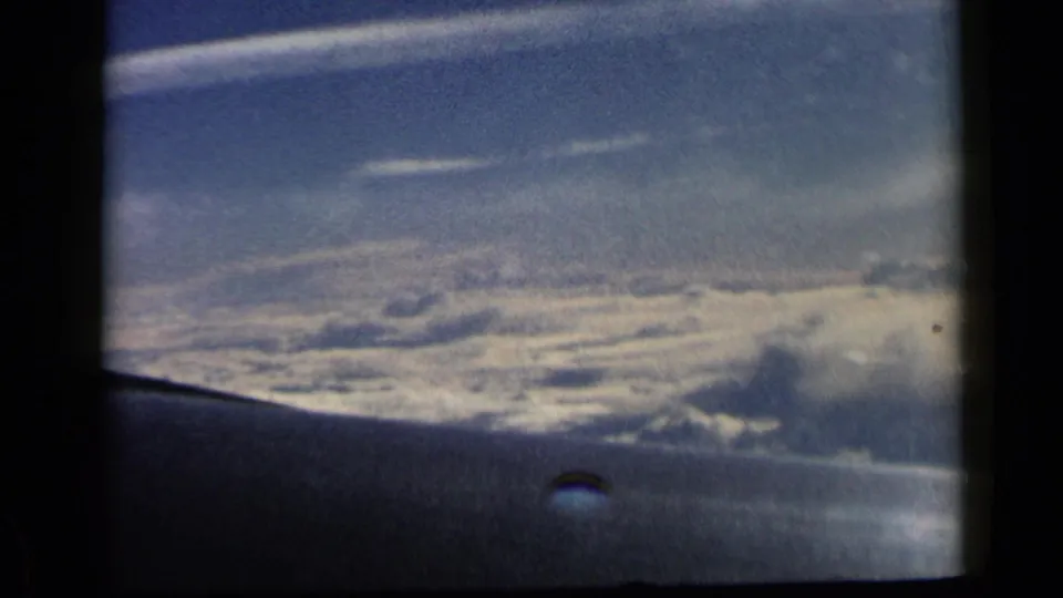 1960 8mm airplane-window shot with the wing visible at bottom and a broad, softly exposed cloudscape across the horizon.