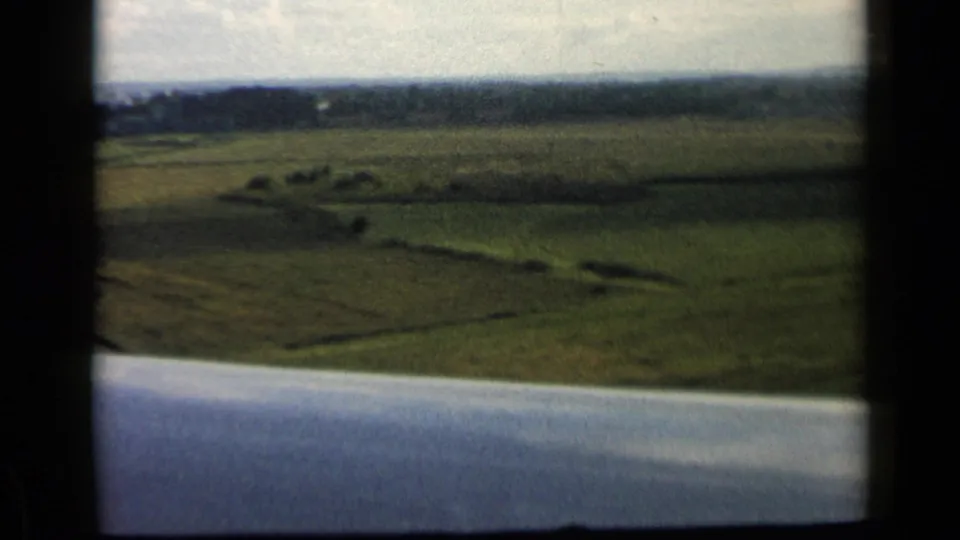 Low aerial view over green fields near the reported Vatican, Italy location, with an airplane wing crossing the lower frame.