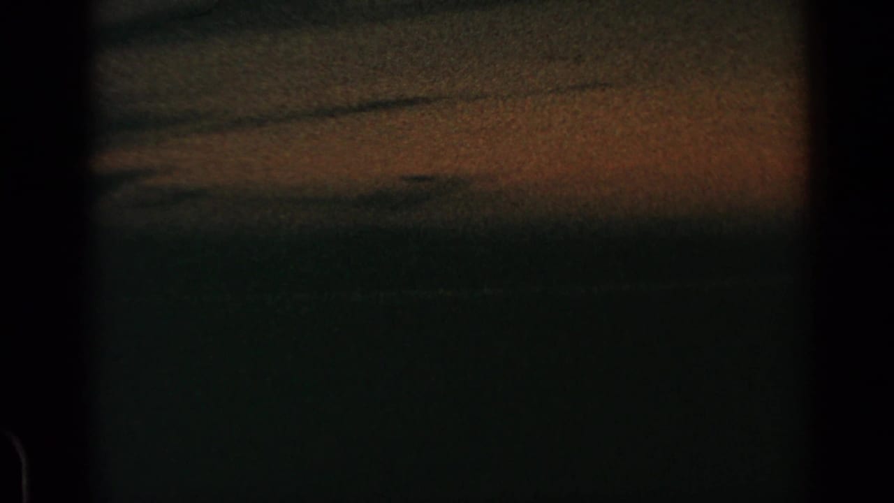 Dark grainy sky with a muted orange band near the horizon and black film borders.
