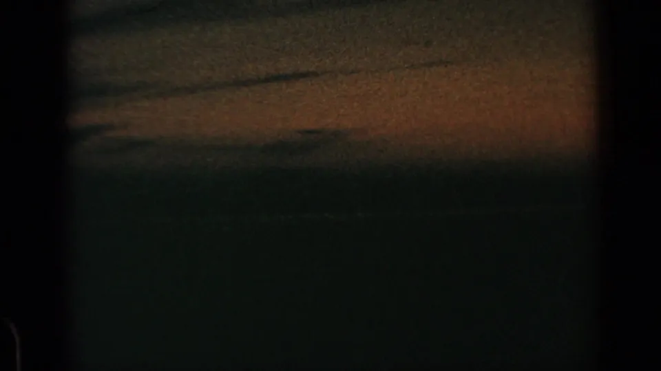 1960 8mm home-movie frame showing a dark sky, faint warm horizon color, heavy grain, and visible film-edge borders.
