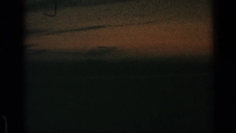 1960 8mm frame with a low-light sky, subdued orange-brown horizon, visible grain, and dark film-edge framing.