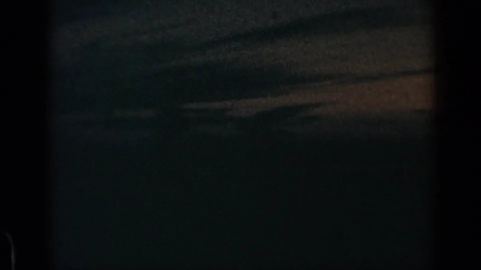 1960 8mm home-movie frame showing a dark blue-green sky, faint horizontal light band, and textured low-light exposure.